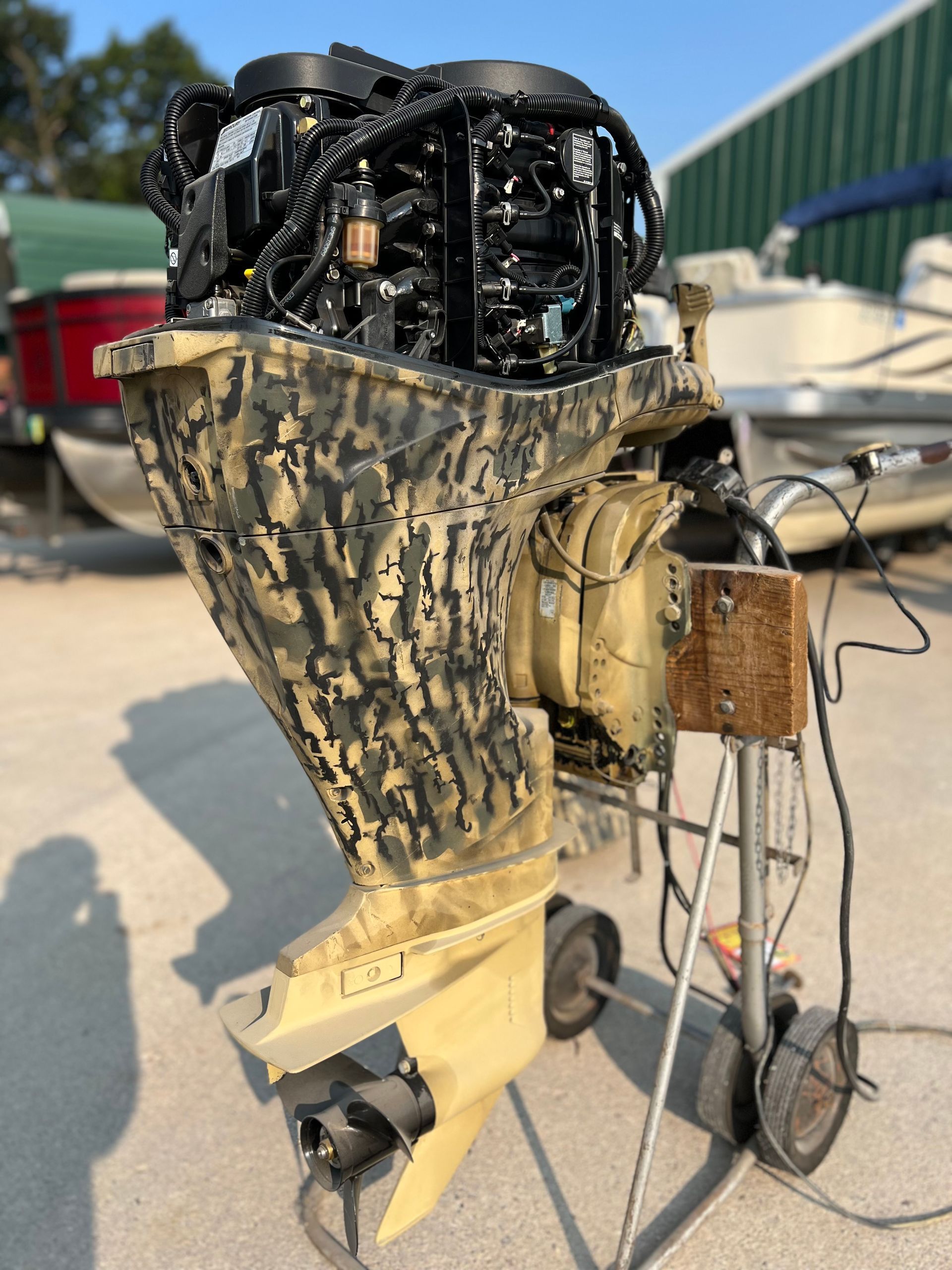 Outboard motor with camouflage cover, sitting on a wheeled stand outdoors.