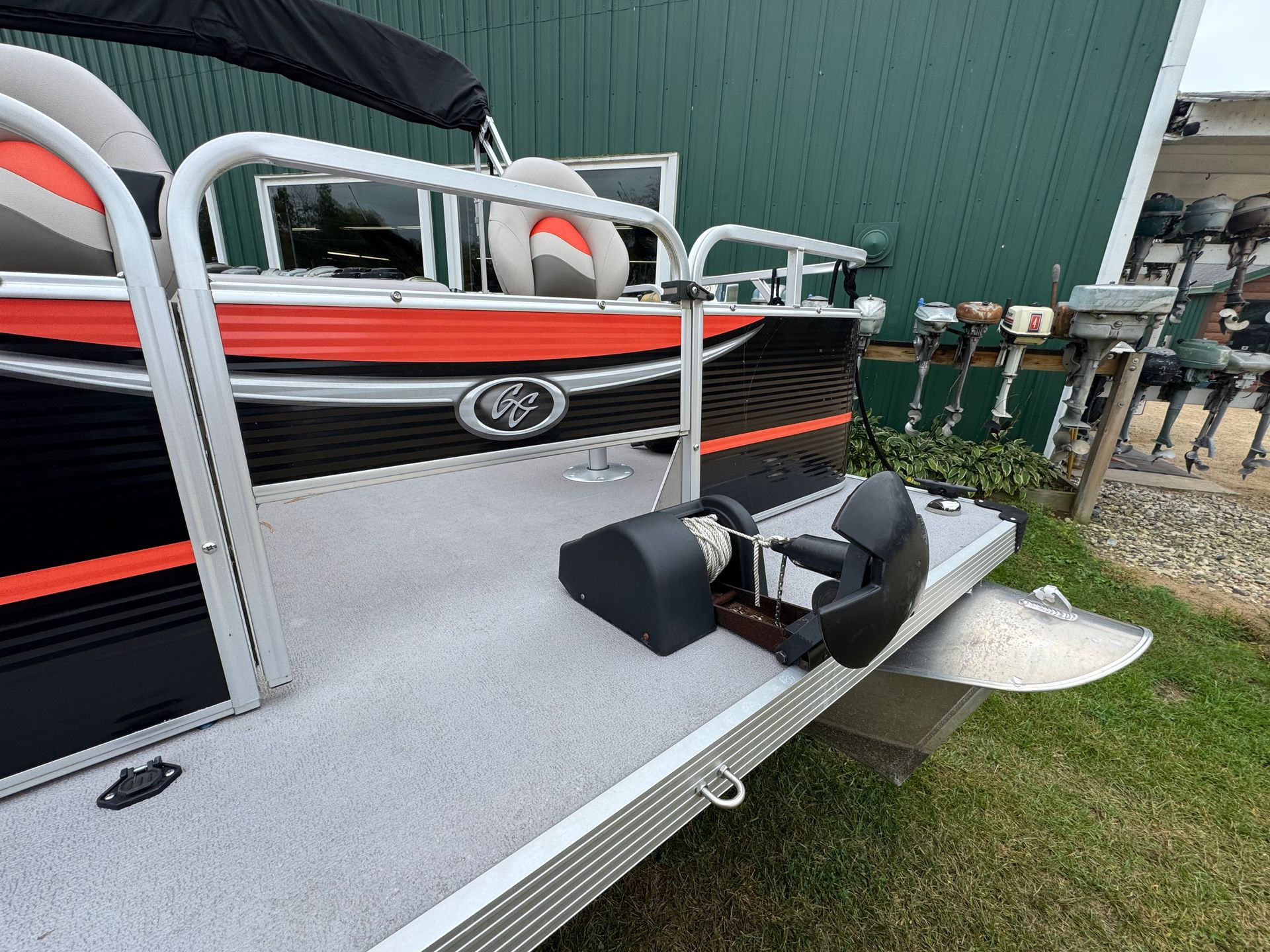 A pontoon boat with black, orange, and silver accents is docked near a green building.