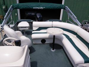 The inside of a pontoon boat with green and white seats and a table