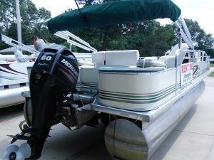 A pontoon boat with a mercury engine is parked in a parking lot.