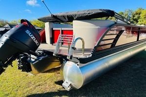 A pontoon boat with a suzuki outboard motor is parked in the grass.