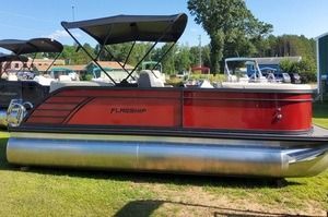 A red pontoon boat with a canopy is parked in a grassy field.