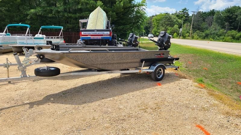 A boat is parked on a trailer in a gravel lot.