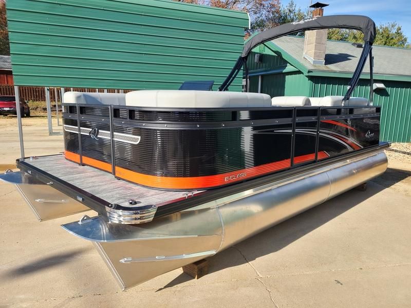 A black and orange pontoon boat is parked in front of a green building.