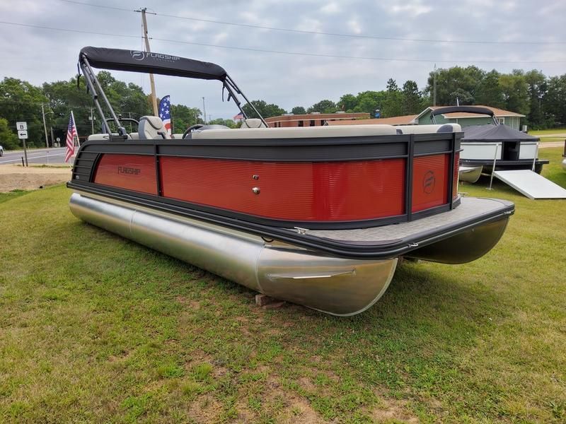 A red and black pontoon boat is sitting on top of a lush green field.
