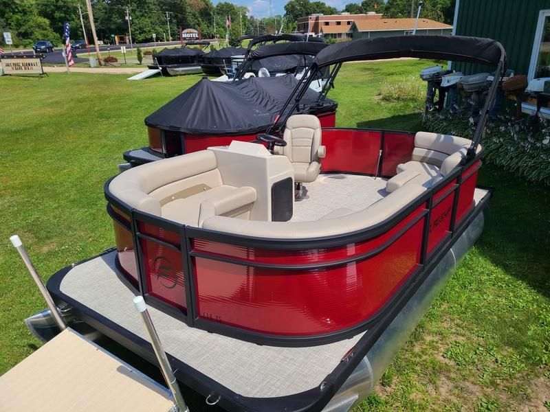 A red pontoon boat is parked in the grass next to a dock.