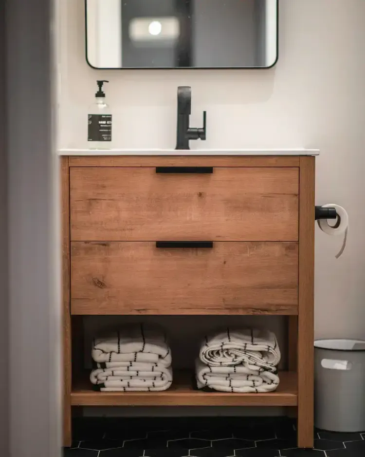 Modern bathroom vanity with wood drawers, black faucet, mirror, soap dispenser, and towels underneath