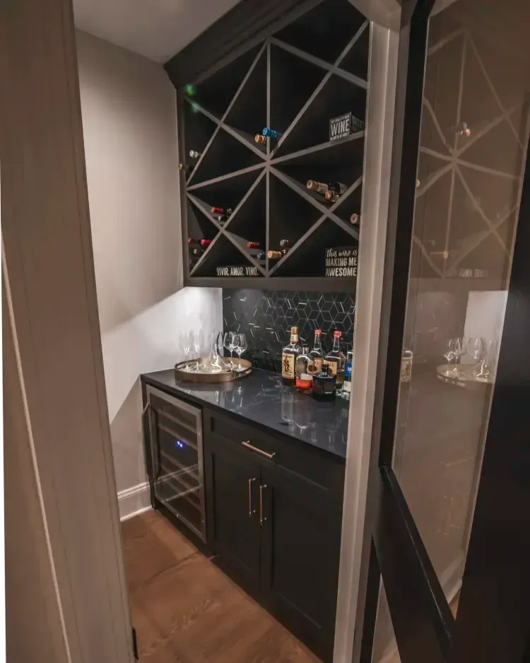 Built-in black home bar with wine rack, glass cabinet, countertop drinks, and mini fridge