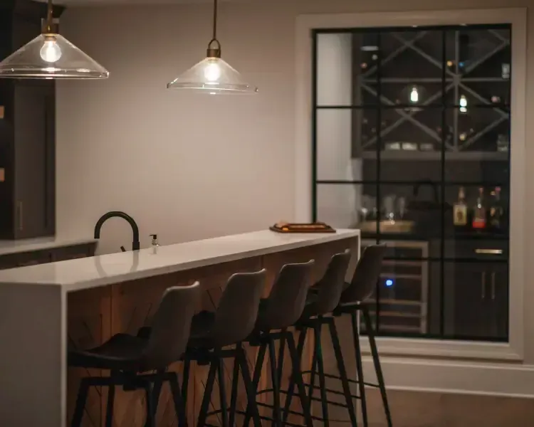 Modern kitchen with island, bar stools, pendant lights, and a wine cooler by a window