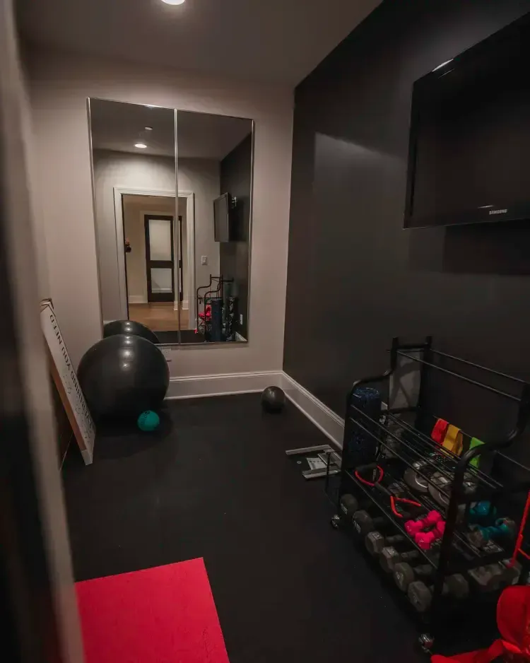 Narrow home gym hallway with exercise ball, mirror, weights rack, and black floor mats