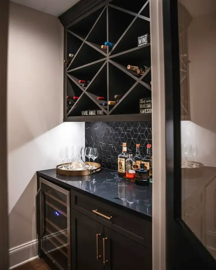 Built-in black bar cabinet with wine rack, glass shelves, and bottles in a modern alcove