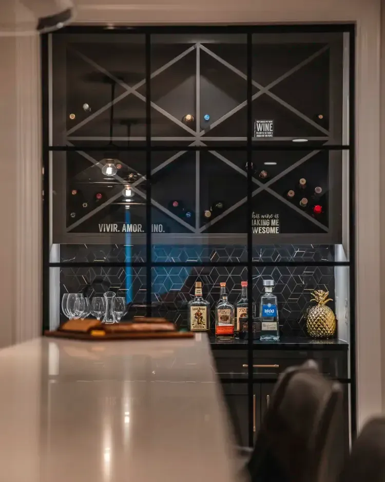 Wine rack with bottles and glasses behind a table in a dimly lit bar or dining room
