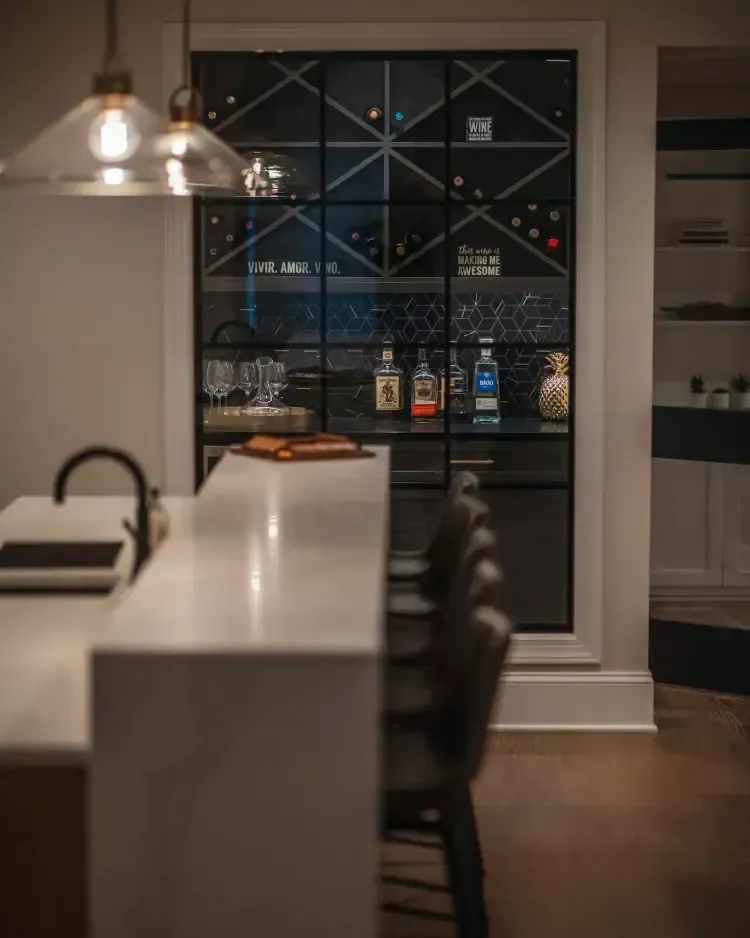 Modern kitchen with white island, black bar stools, and a glass wine display in the background