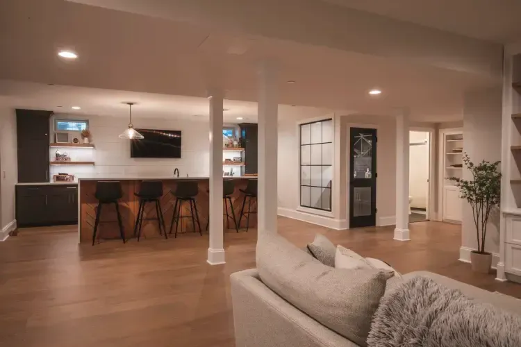 Open-plan living room with kitchen island, bar stools, white columns, and wood floors