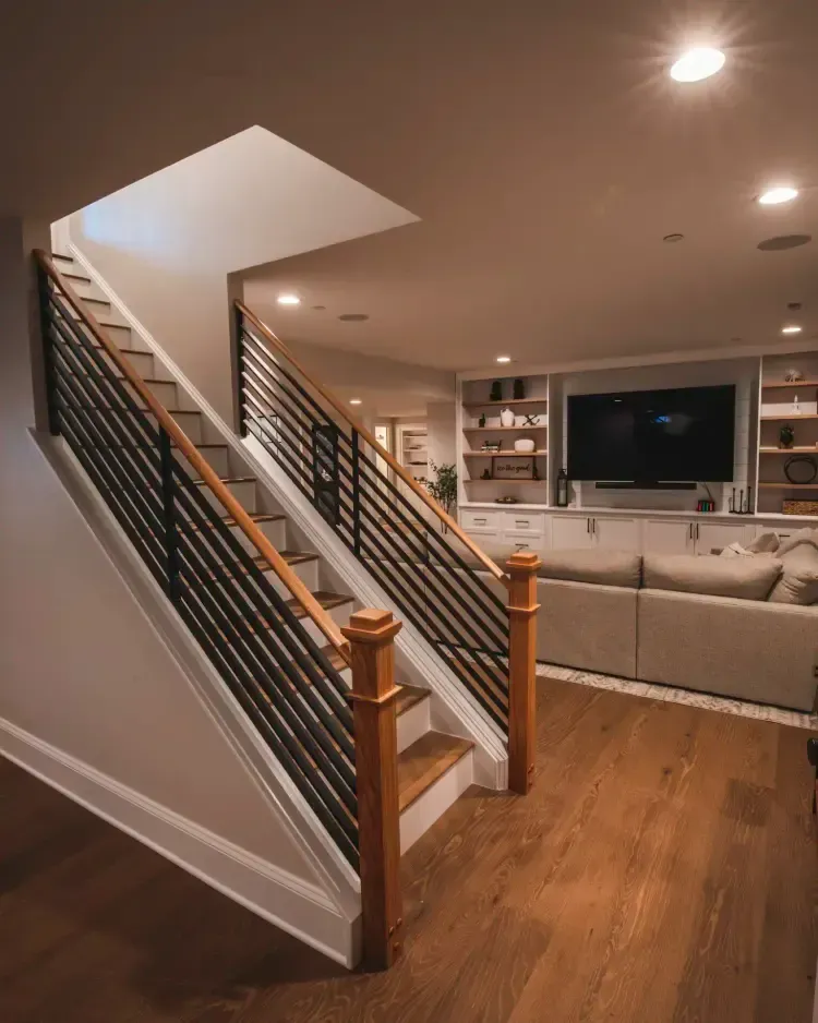 Staircase with black railing leading to a cozy living room with a TV, beige sofa, and hardwood floors.