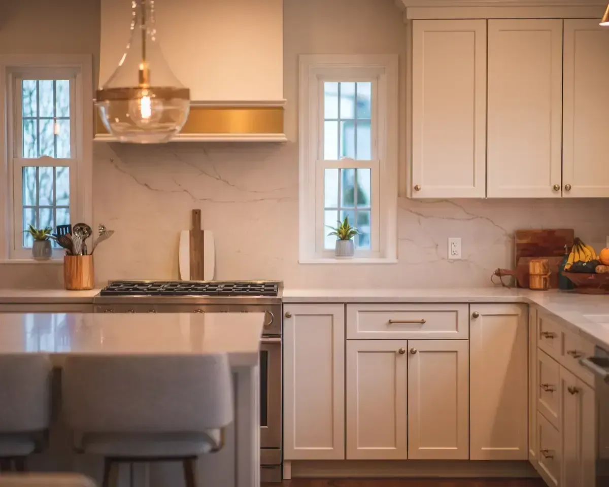 Modern kitchen with white cabinets, marble backsplash, island seating, and brass pendant light.