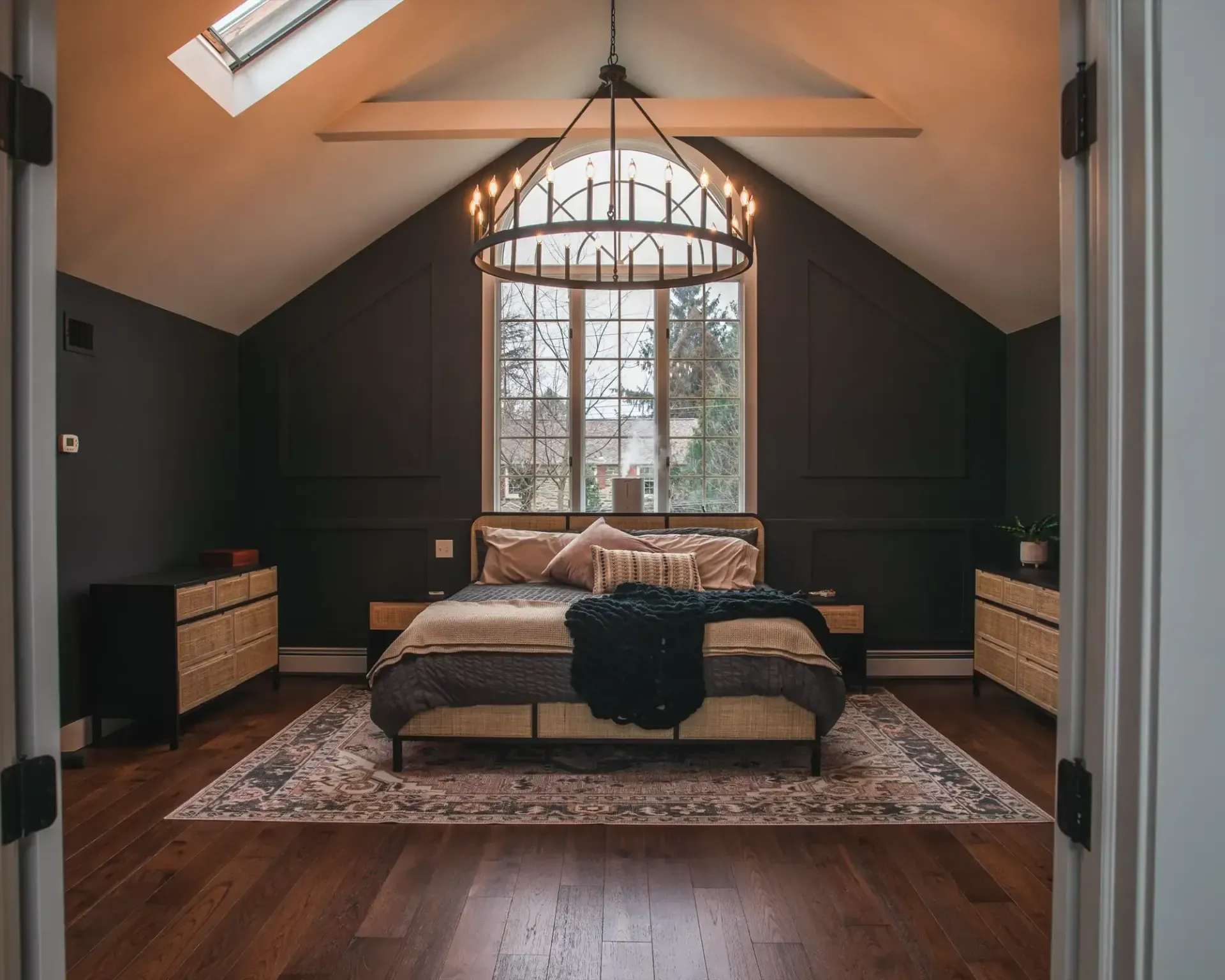 Cozy bedroom with a large bed, skylight, arched window, dark walls, and wooden floors