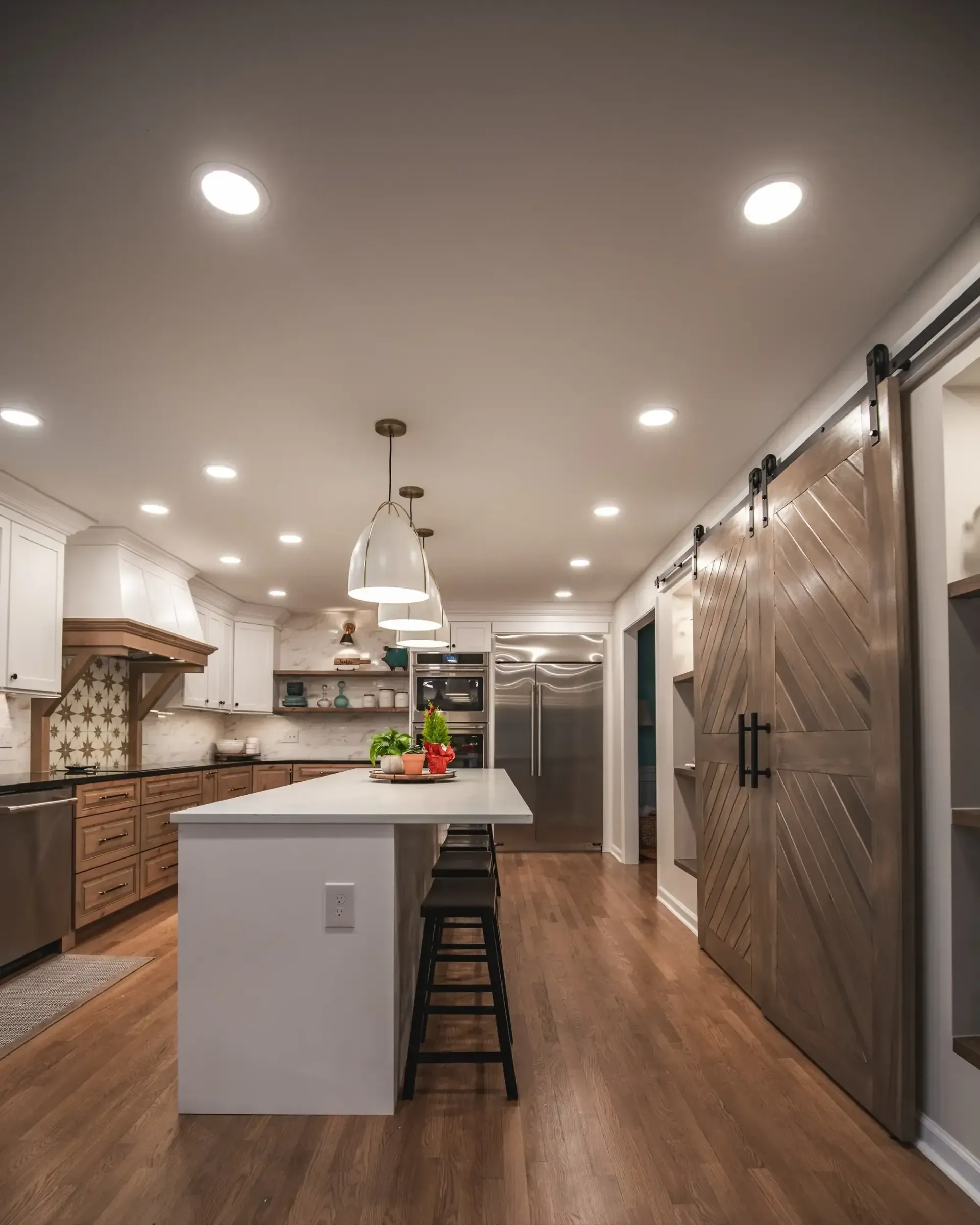 Modern kitchen with large island, pendant light, wooden floors, and stainless steel appliances, viewed from dining area