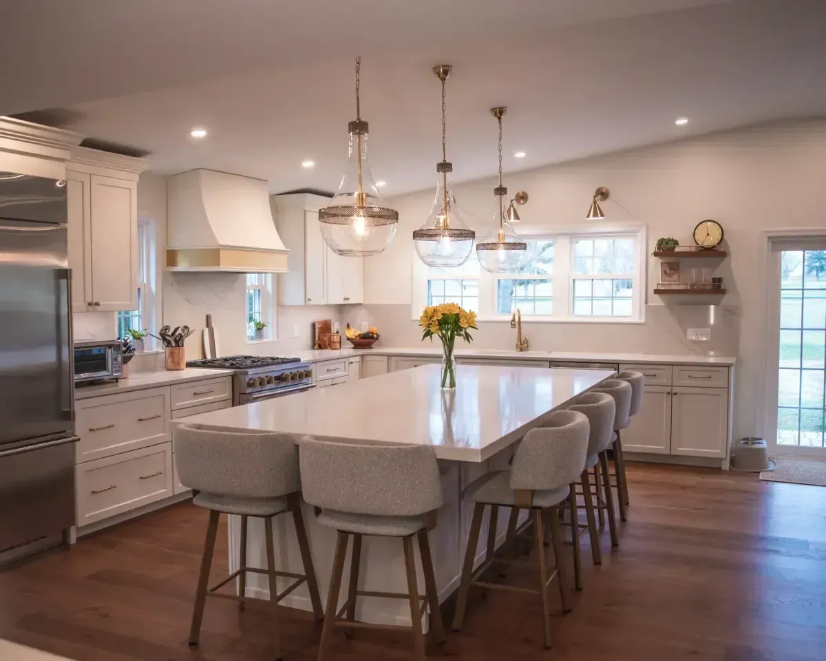 Bright modern kitchen with a large island, pendant lights, and gray barstools on wood floors.