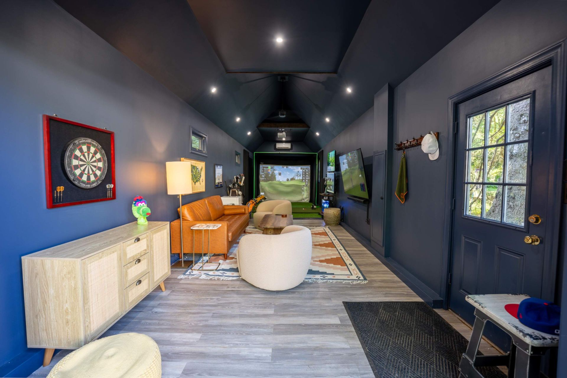 Narrow navy hallway with dartboard, chairs, desk, rug, and front door with windows