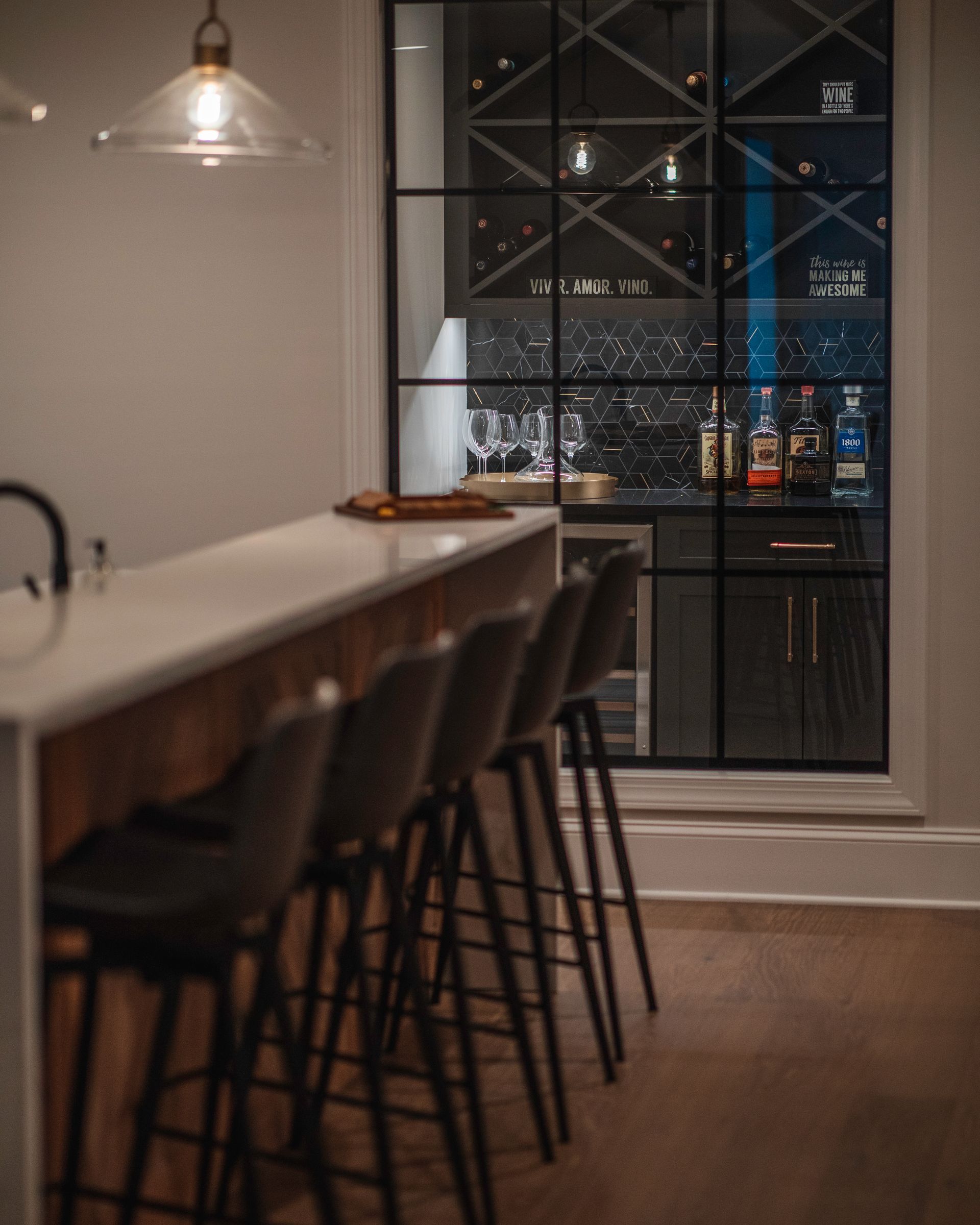 Modern kitchen with a long island, bar stools, pendant light, and glass cabinet shelves with bottles