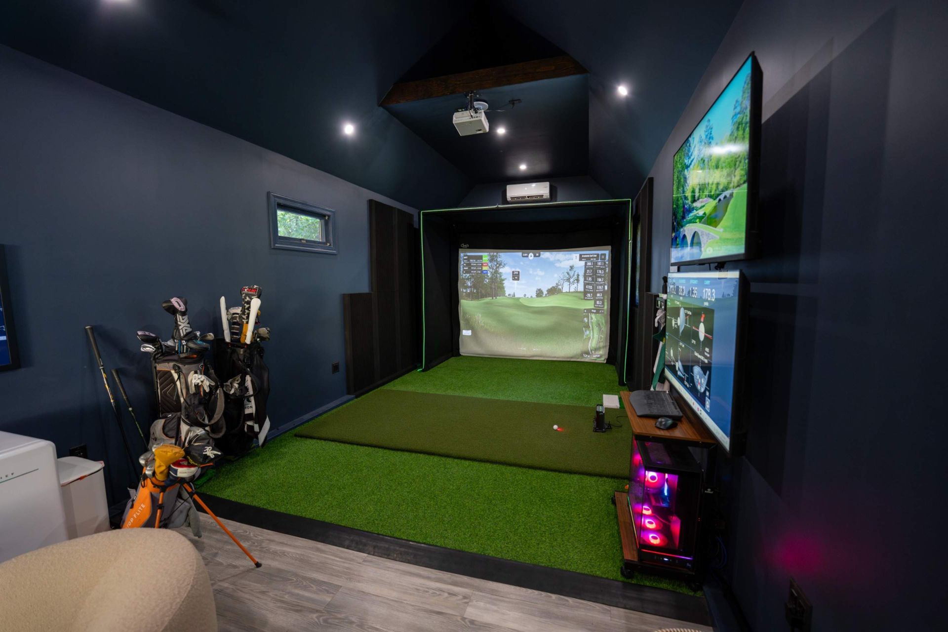 Indoor golf simulator room with screens, green turf, and golf clubs in a dark, modern setup