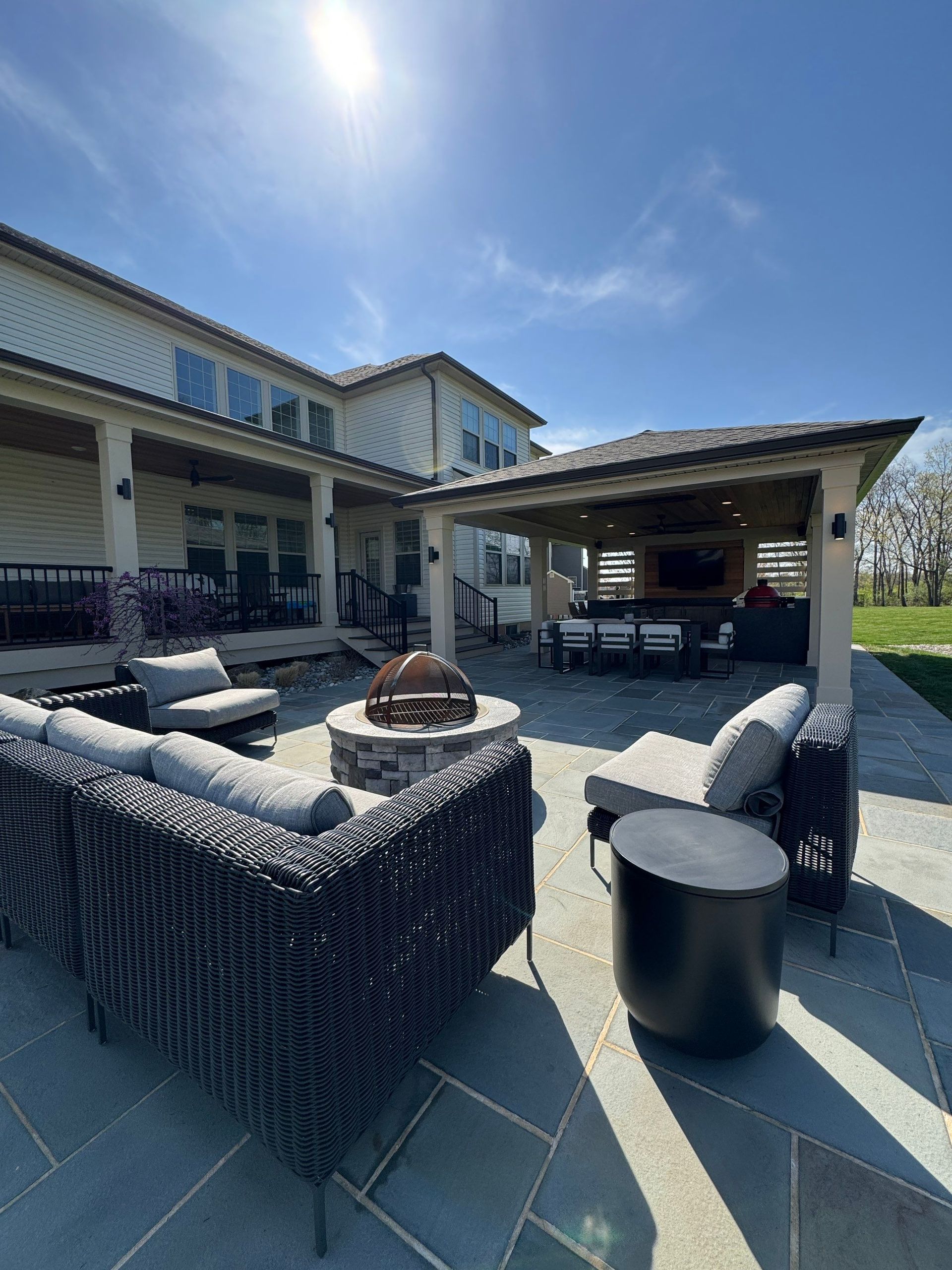 Outdoor patio with wicker seating, fire pit, and covered lounge area under a bright blue sky