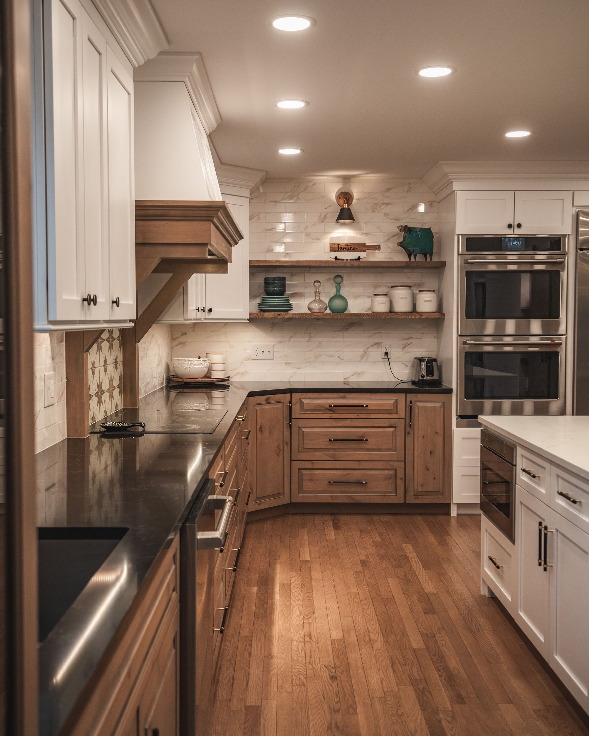 Bright modern kitchen with white cabinets, wood floors, dark counters, and built-in double ovens.