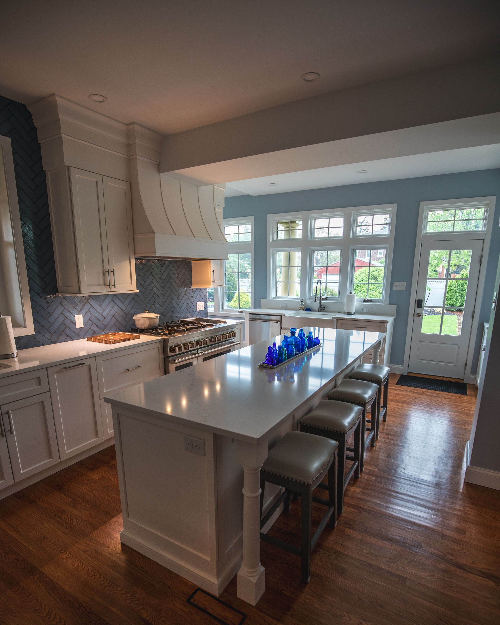 Bright white kitchen with island, barstools, hardwood floors, and large windows and doors to a patio.