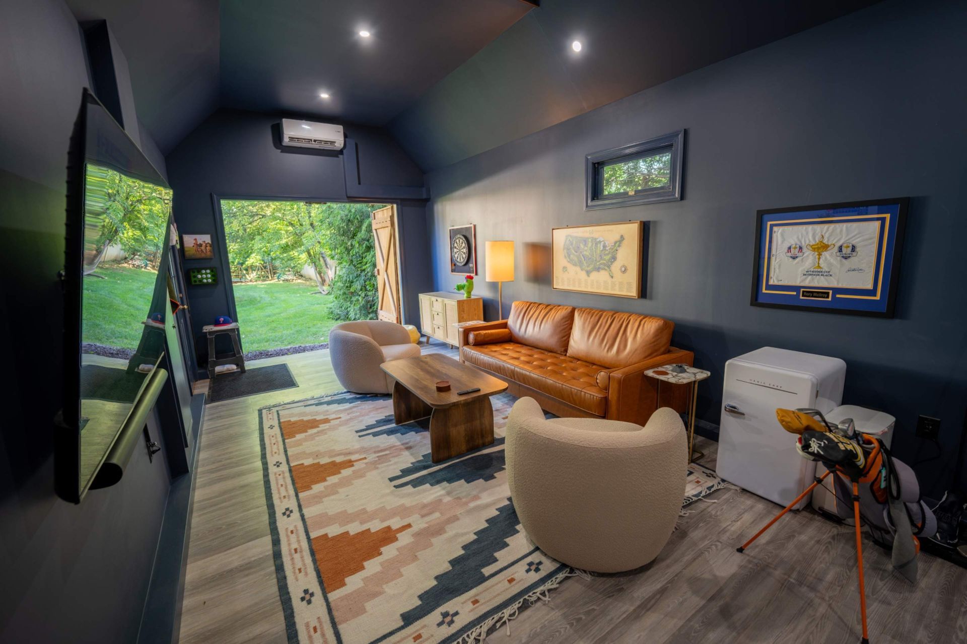 Bright modern living room with orange sofa, beige chair, rug, TV, and open doors to a green patio