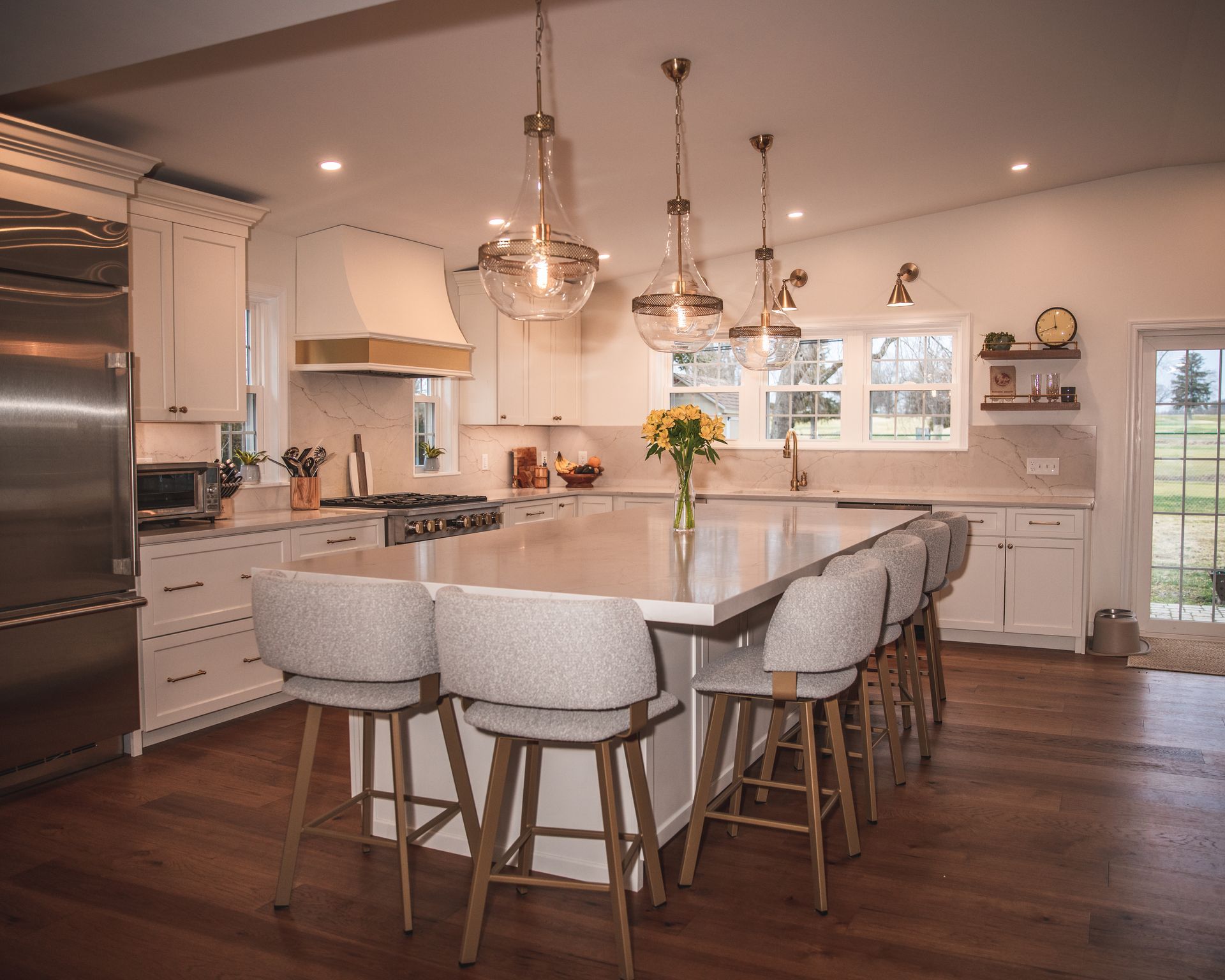 Bright modern kitchen with a large island, white stools, pendant lights, and hardwood floors