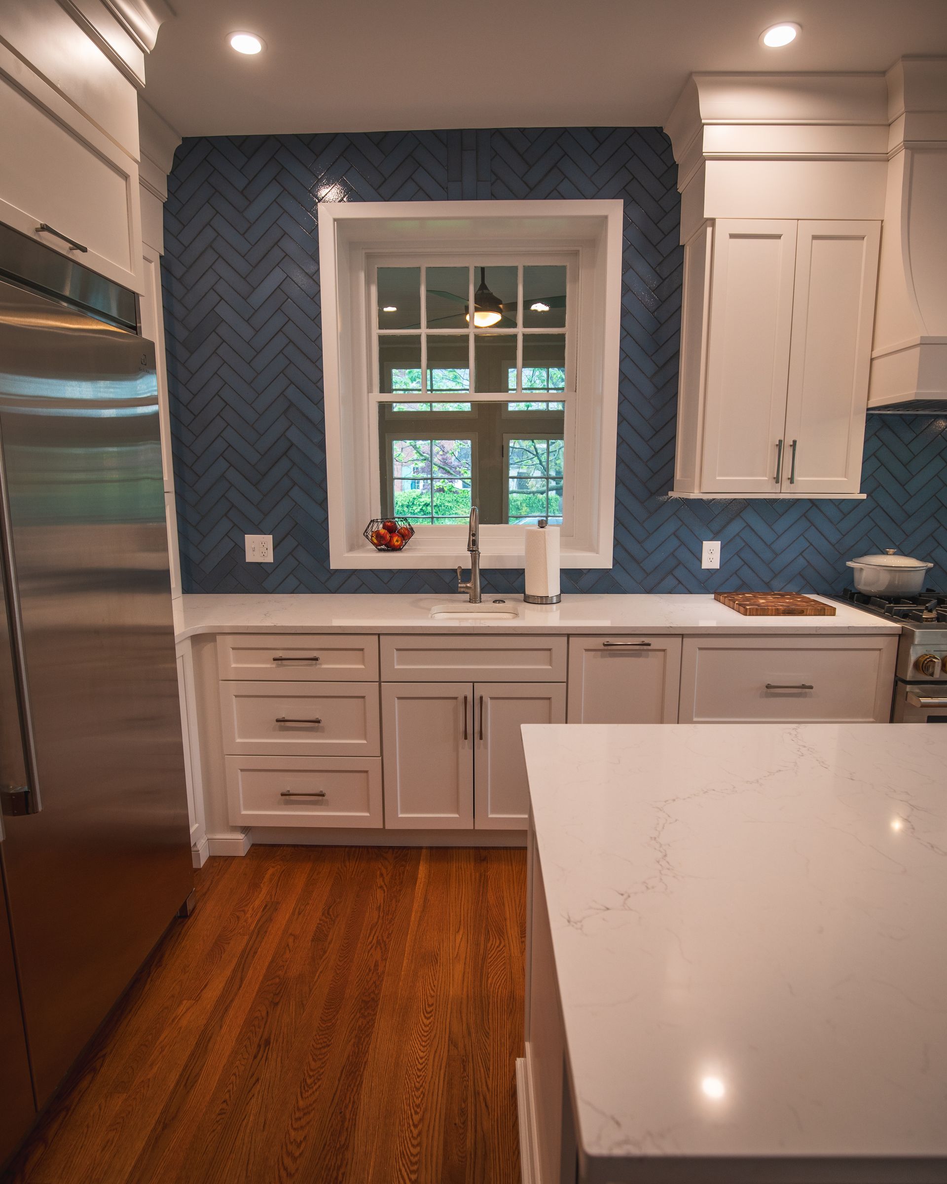 Modern kitchen with blue tile backsplash, white cabinets, stainless fridge, and a window above the sink