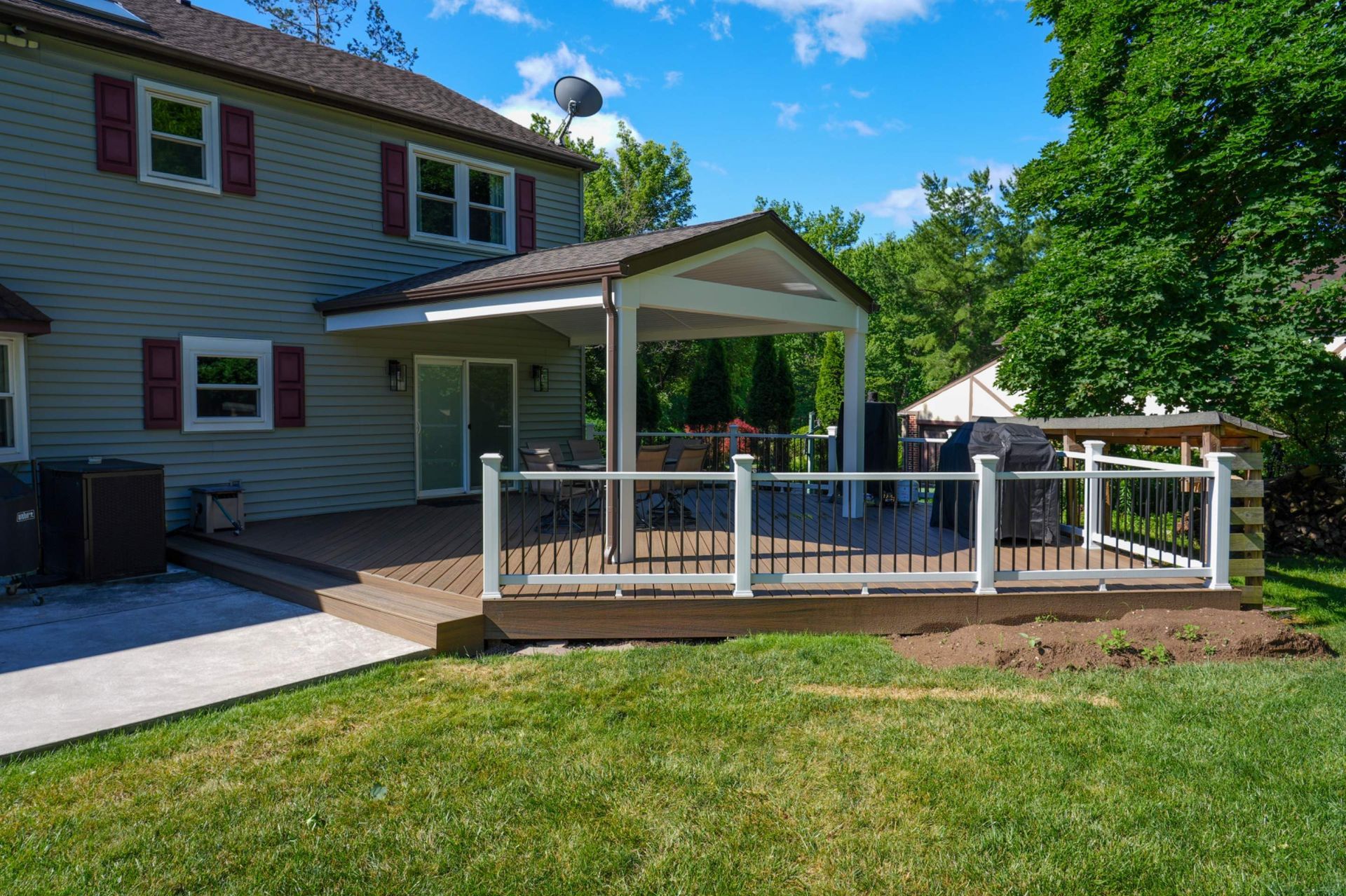 Backyard deck with white railing attached to a house, beside a lawn under a blue sky