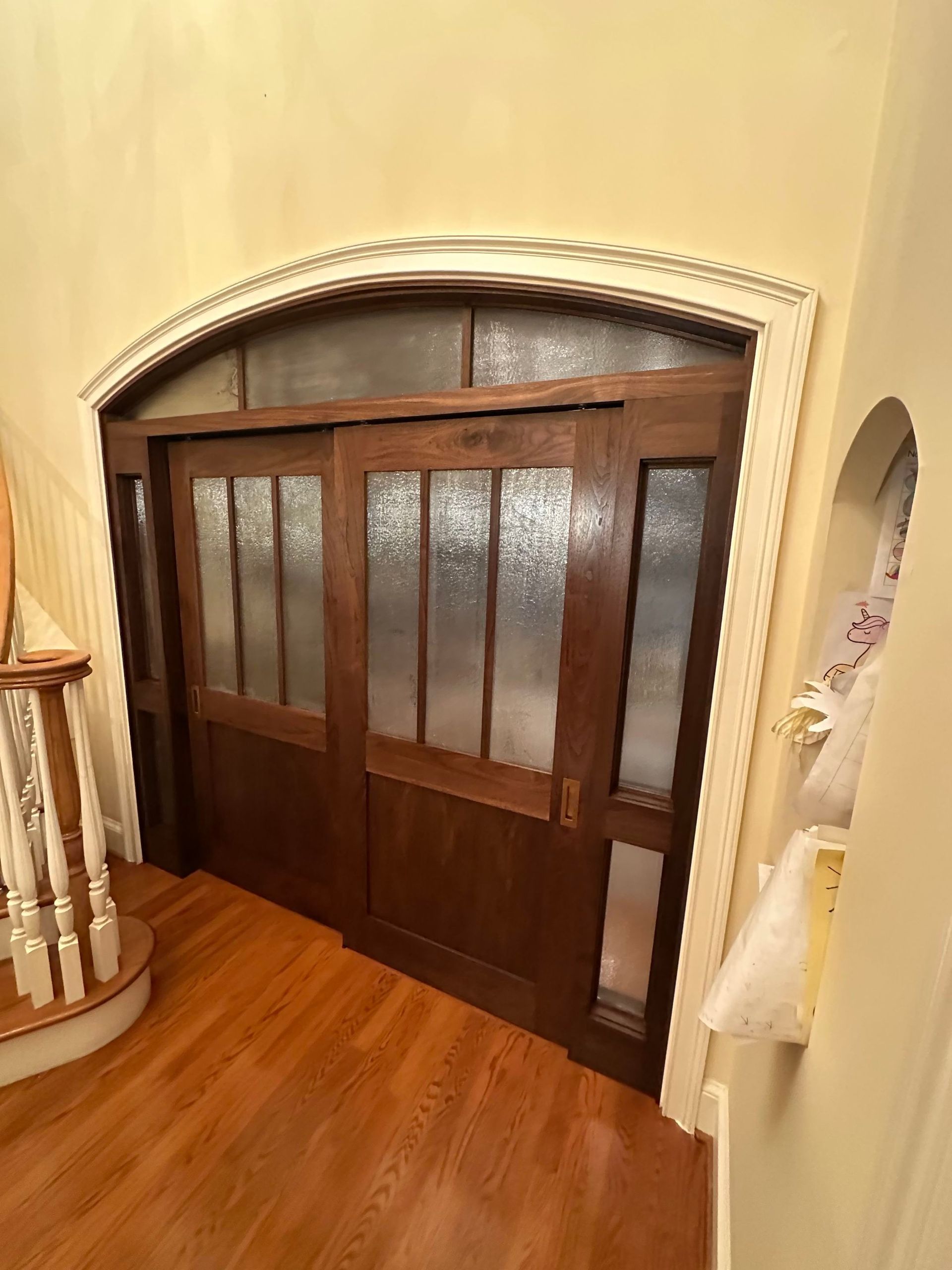 Dark wooden arched doorway with frosted glass panels inside a warm-toned hallway