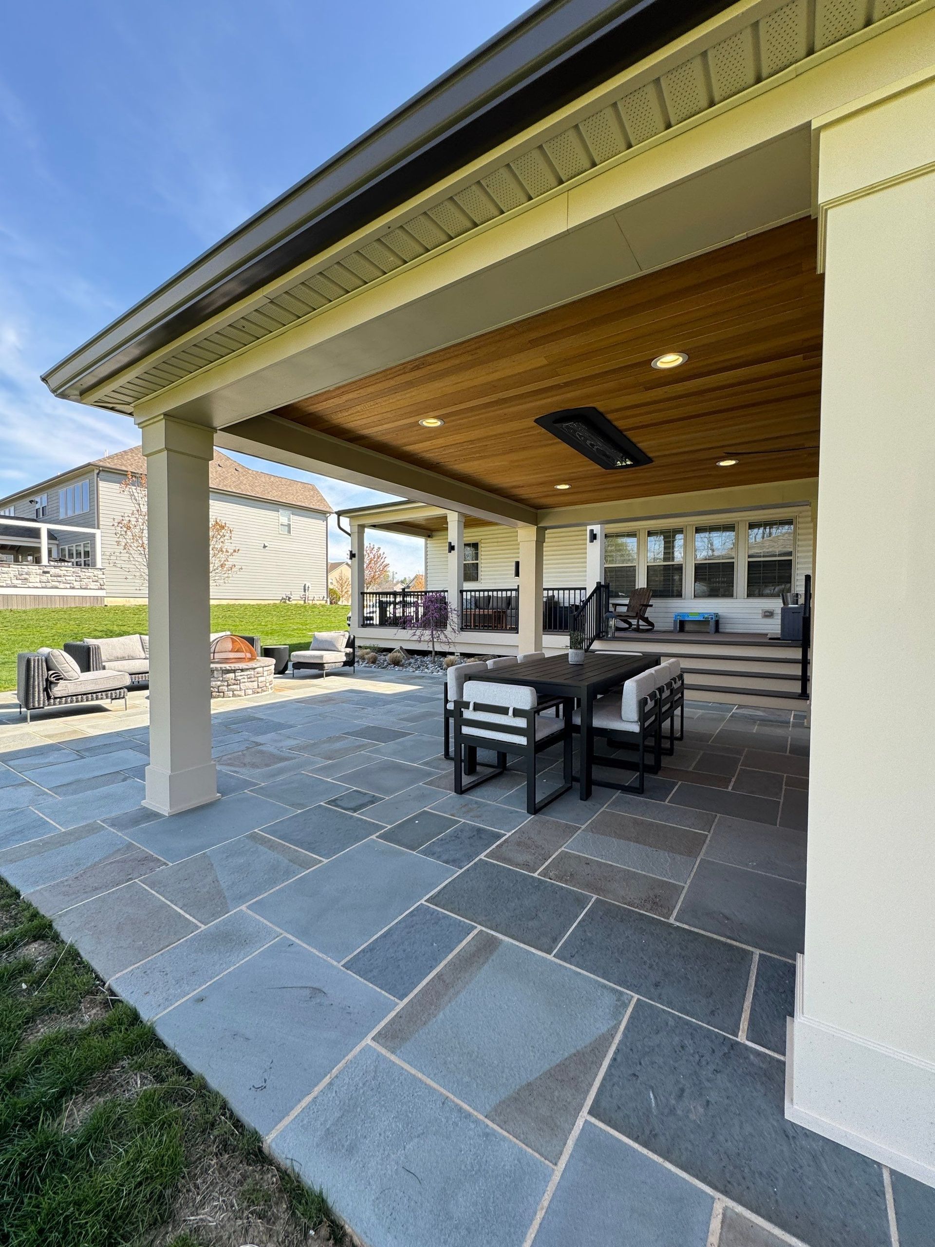 Covered patio with stone pavers, black table and chairs, and a house exterior in the background