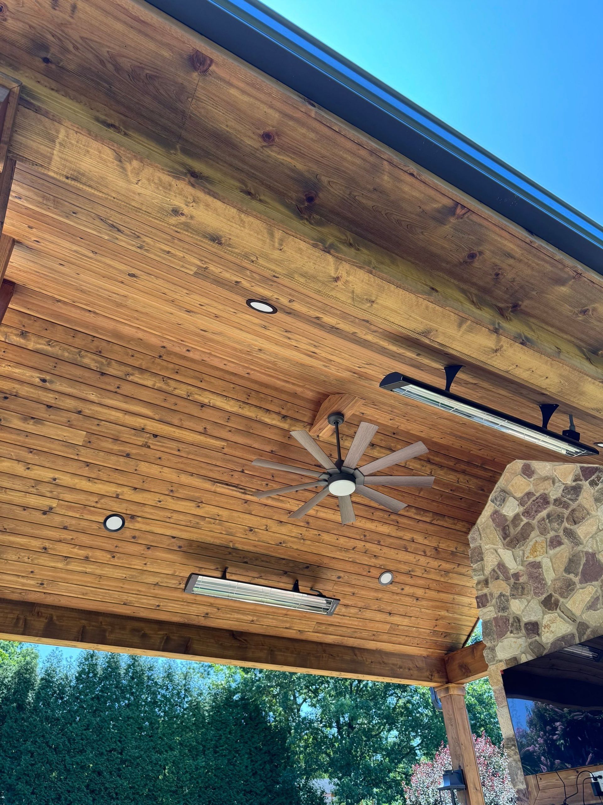 Wooden patio ceiling with ceiling fan, lights, and stone chimney under a covered outdoor space