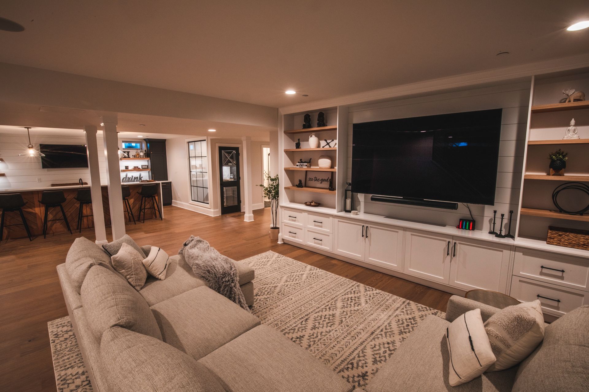 Spacious modern living room with beige sectional, large TV, built-in shelves, and warm lighting