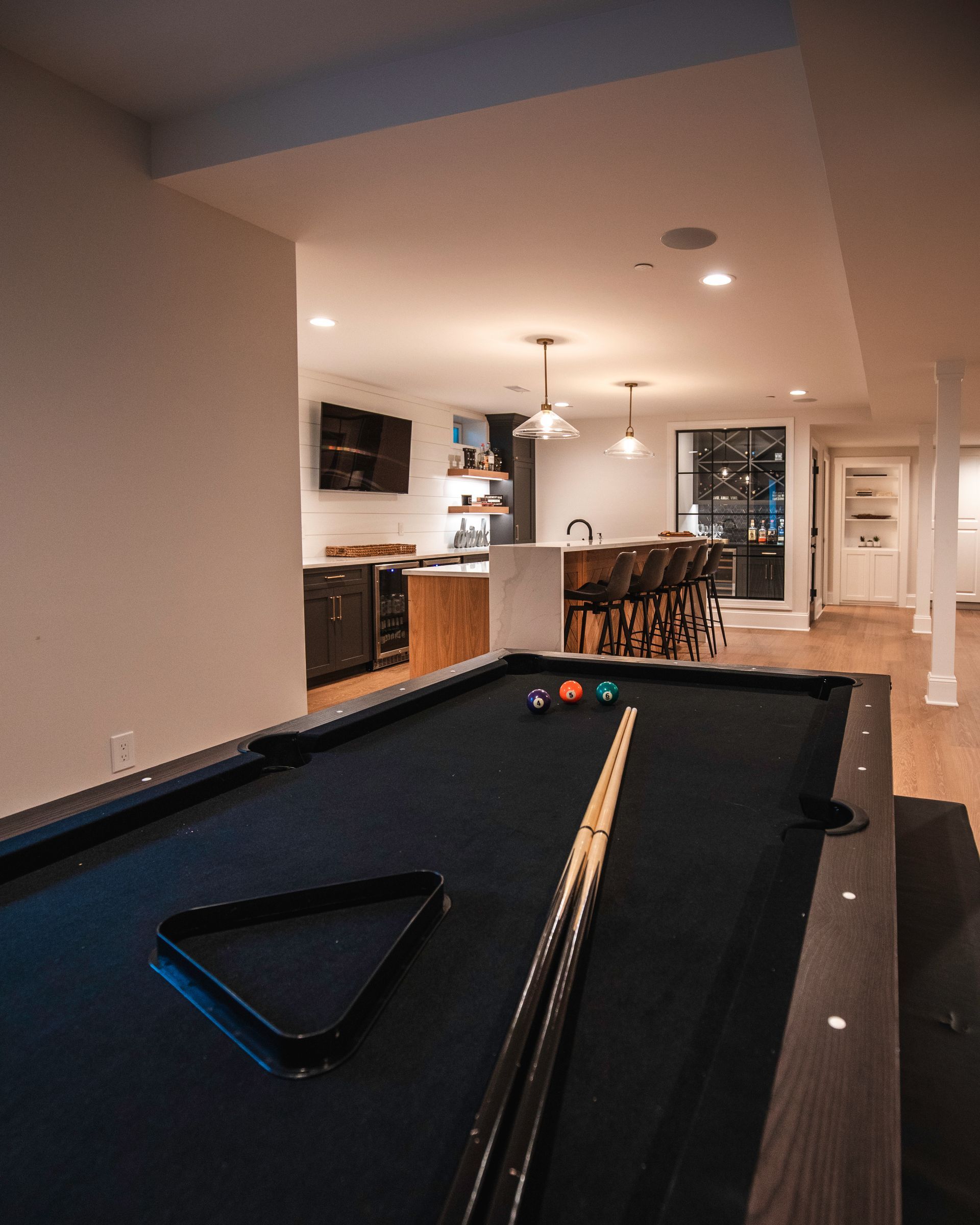 Basement recreation room with a pool table and a bar area in the background.