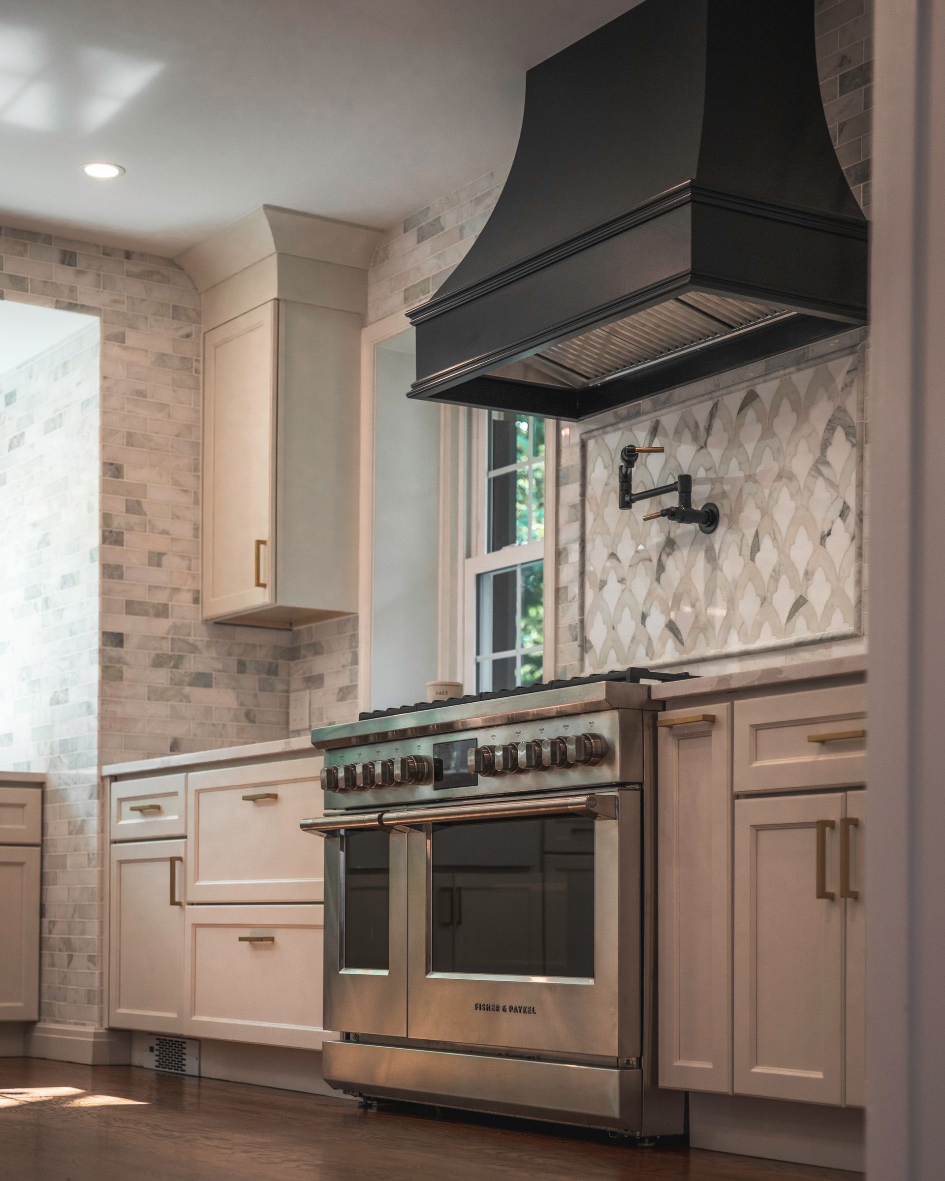 Modern kitchen with stainless range, black hood, and light wood cabinets with patterned tile backsplash
