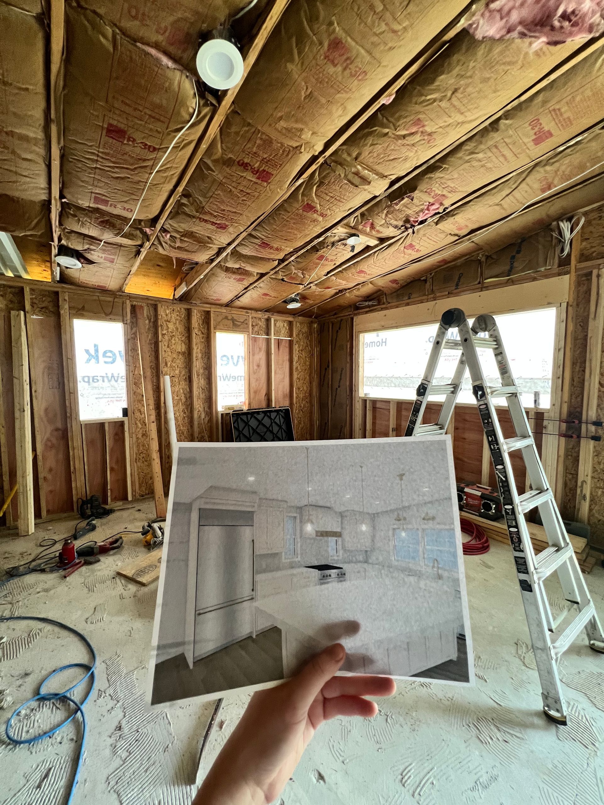 Unfinished room with exposed insulation, ladder, and a hand holding a bathroom design sketch.