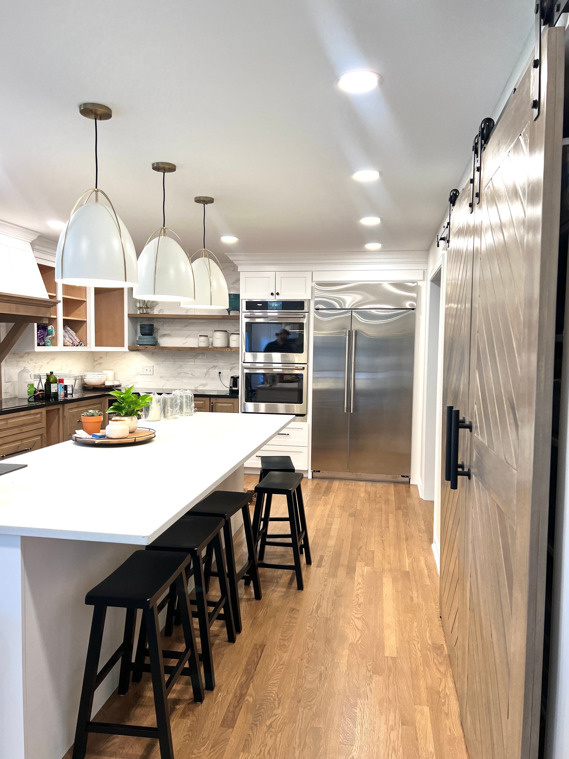 Modern kitchen with a large white island, black stools, pendant lights, and stainless steel appliances