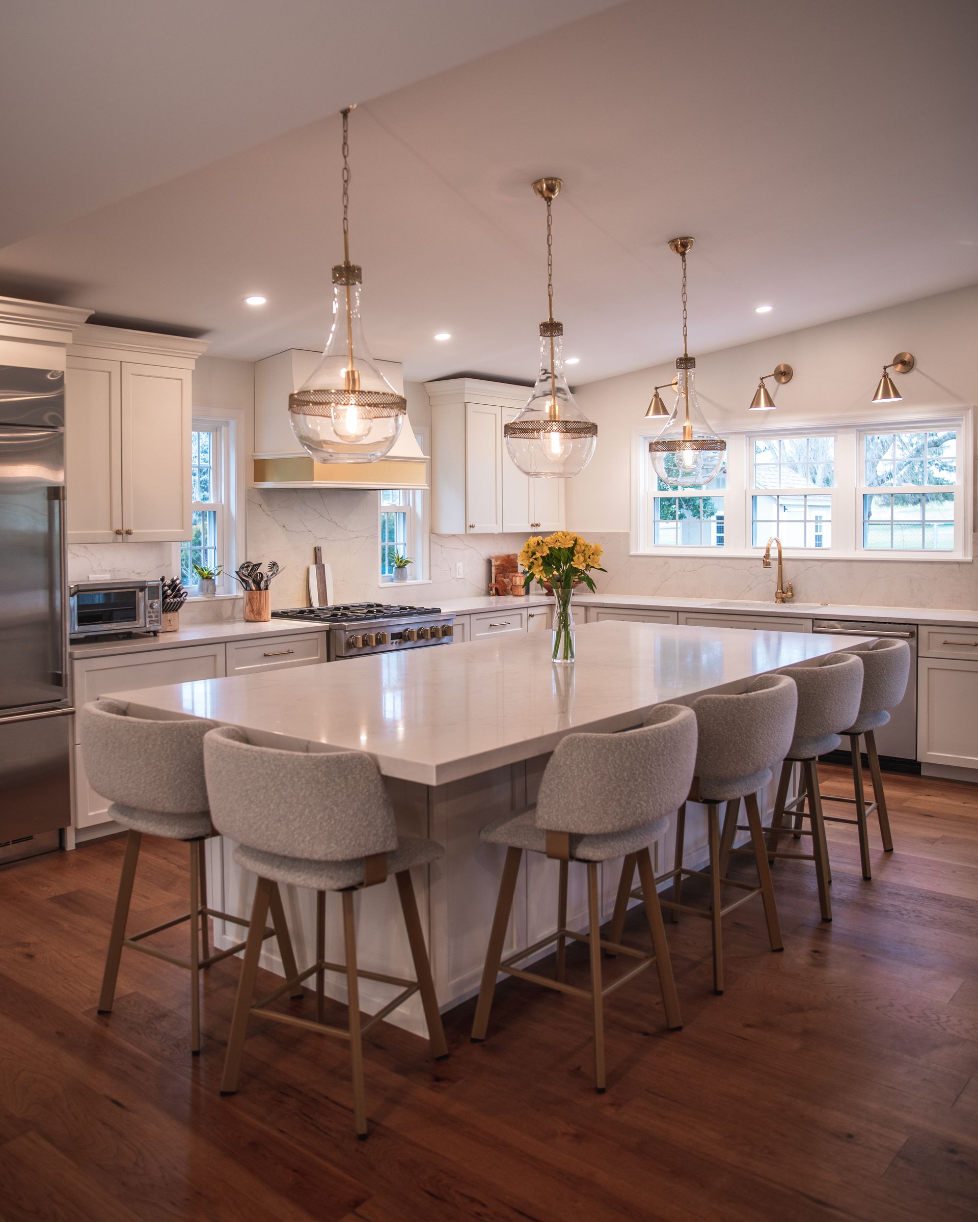 Modern kitchen with a large marble island, pendant lights, and upholstered stools on hardwood floors.