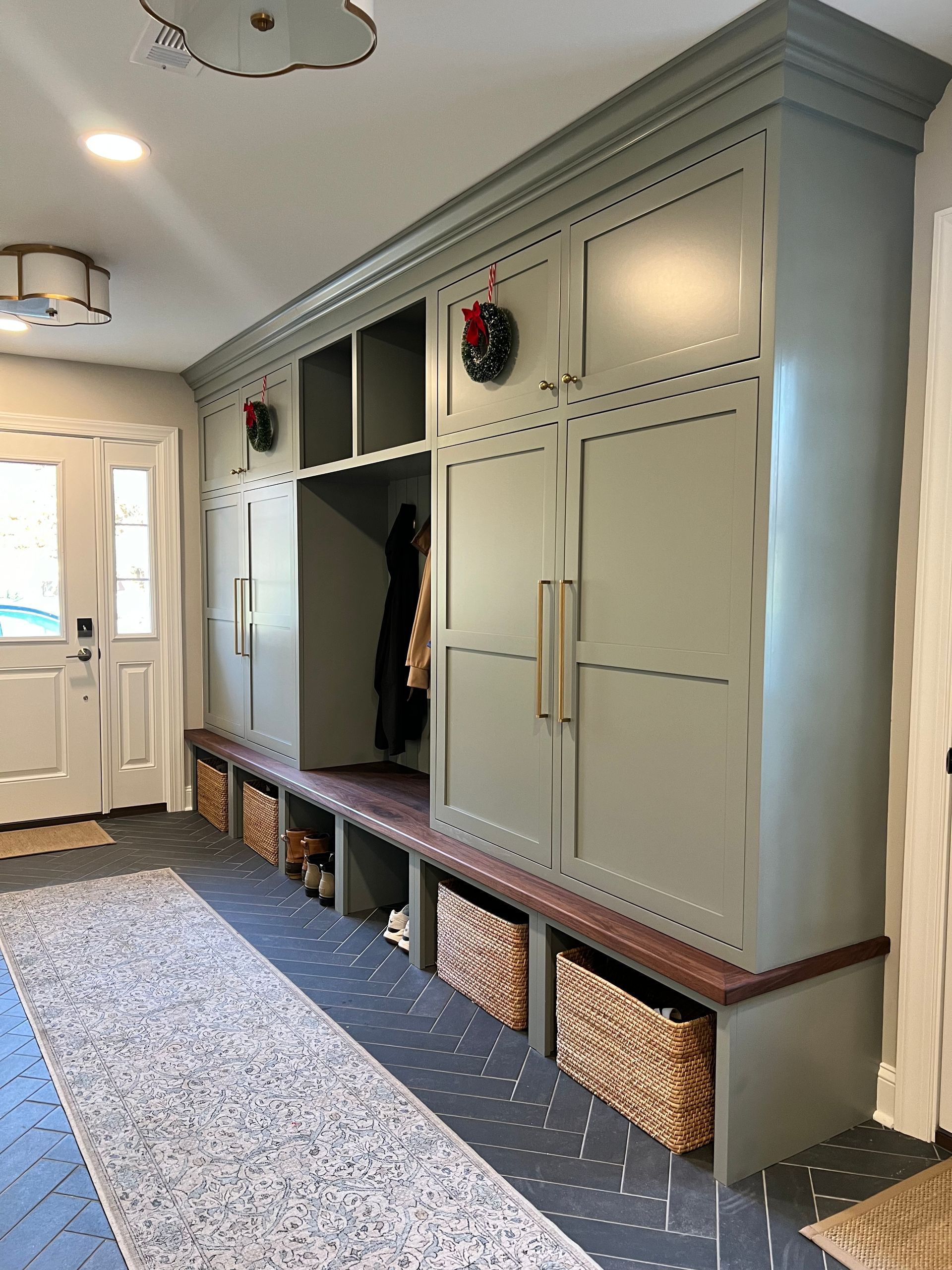 Built-in hallway storage with cream cabinets, dark bench, and woven baskets beside a front door.