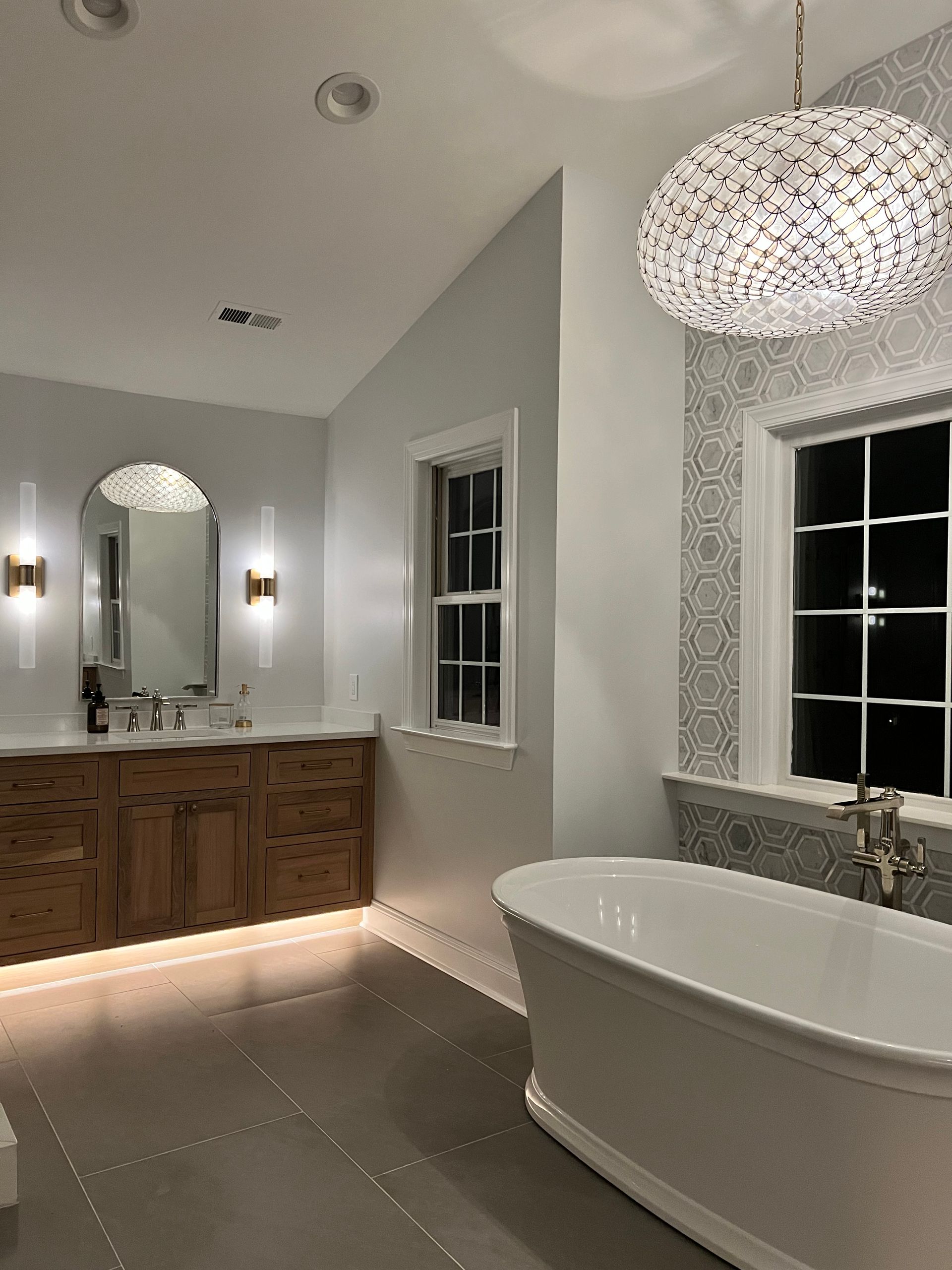 Spacious modern bathroom with double vanity, freestanding tub, large mirror, and pendant light.