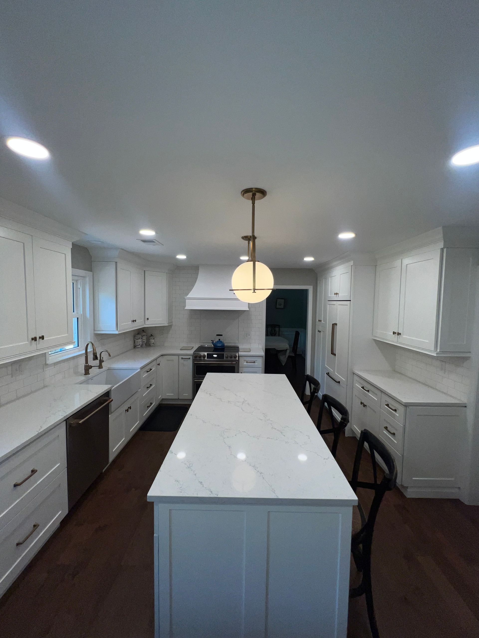 Bright modern kitchen with white cabinets, large island, and pendant light under recessed ceiling lights.