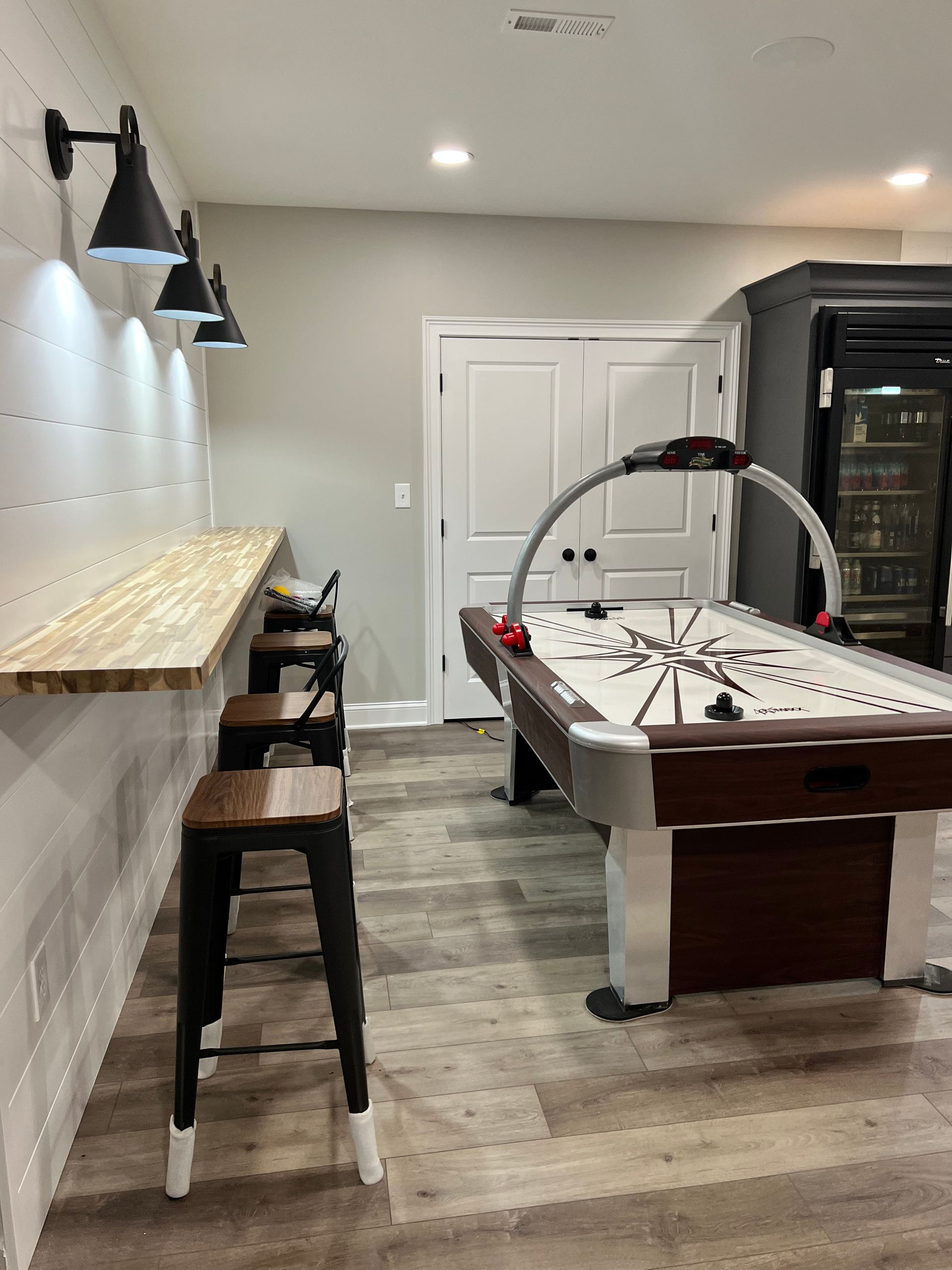 Modern game room with pool table, bar stools, wall lights, and a dartboard on the back wall