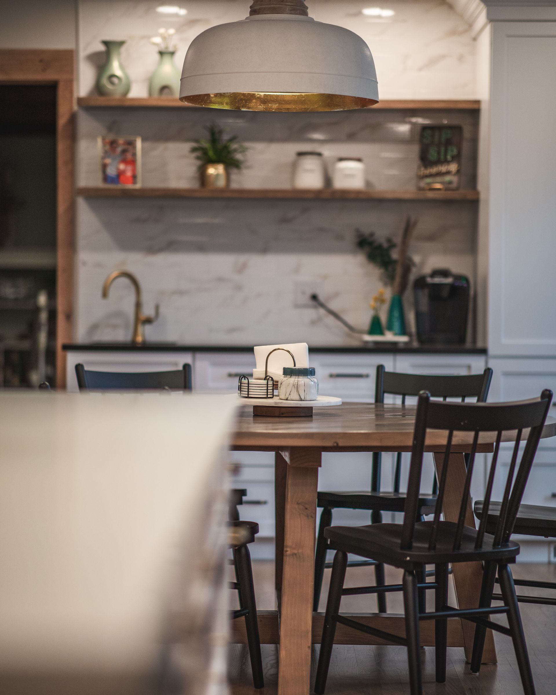 Modern kitchen with wooden dining table, dark chairs, open shelves, and a marble backsplash.