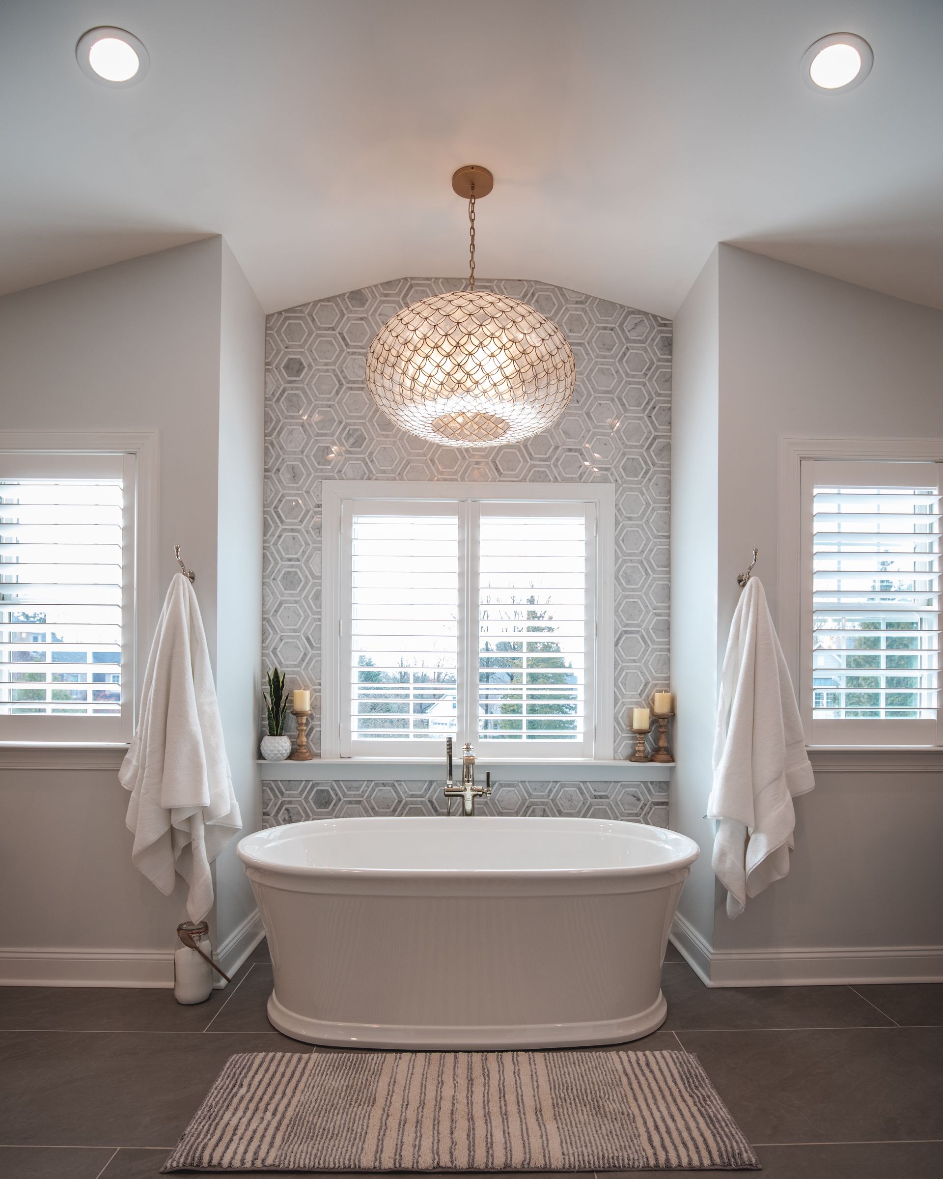 Elegant bathroom with freestanding tub, mosaic backsplash, pendant light, and white towels on both sides
