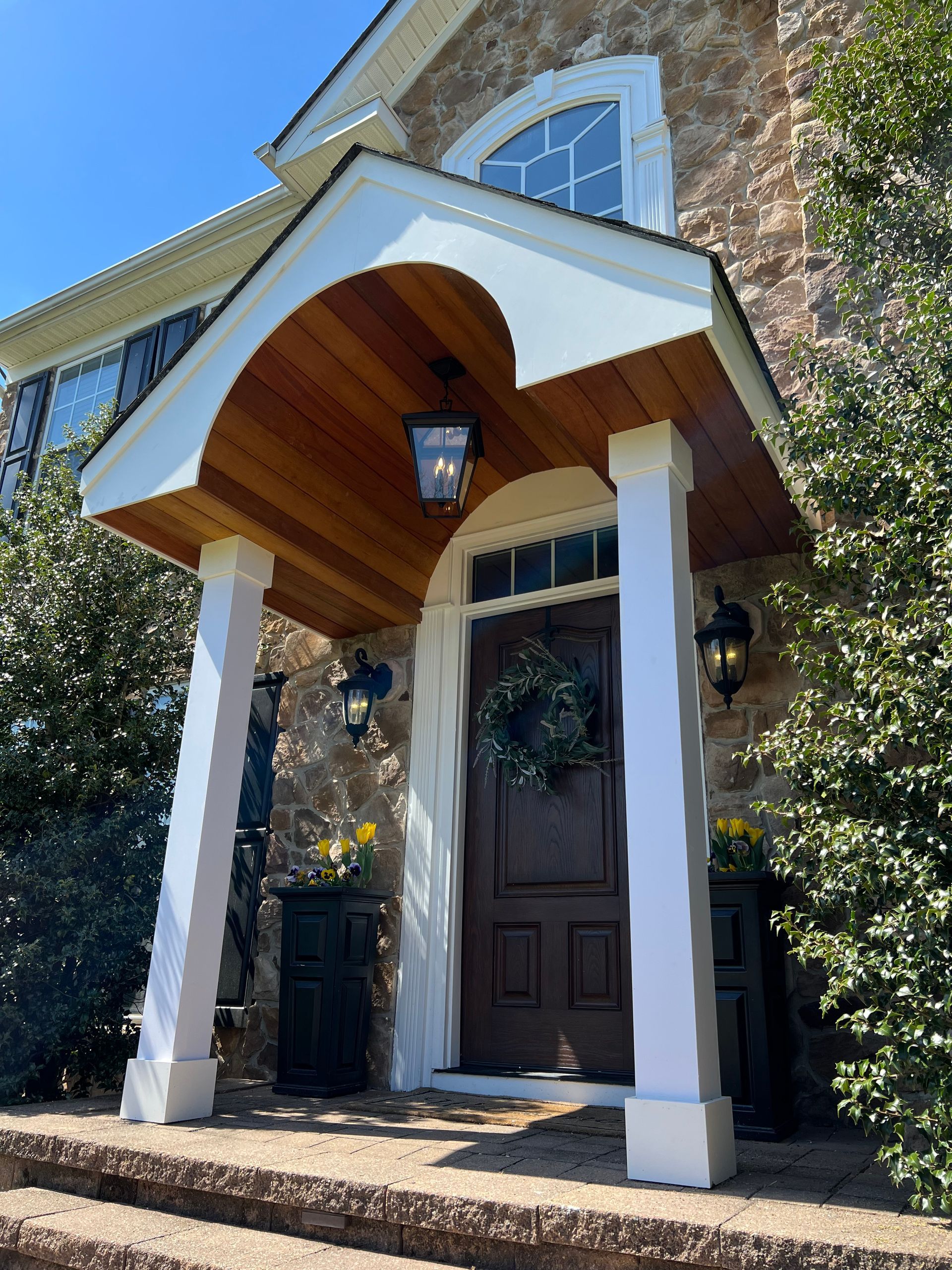 Front porch with white columns, wood ceiling, and dark front door on a brick house