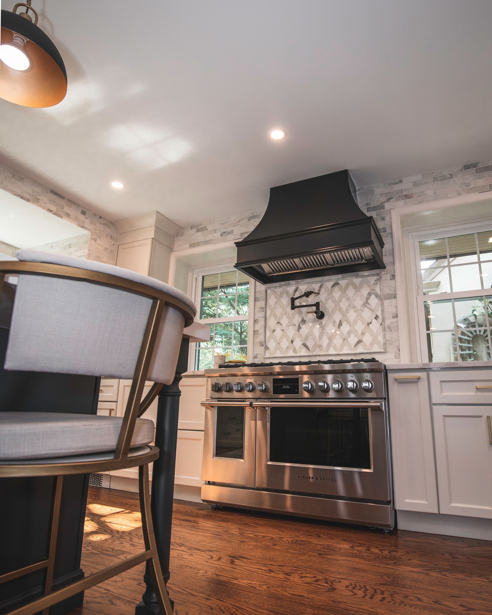 Modern kitchen with stainless steel stove, black range hood, white cabinets, and hardwood floor